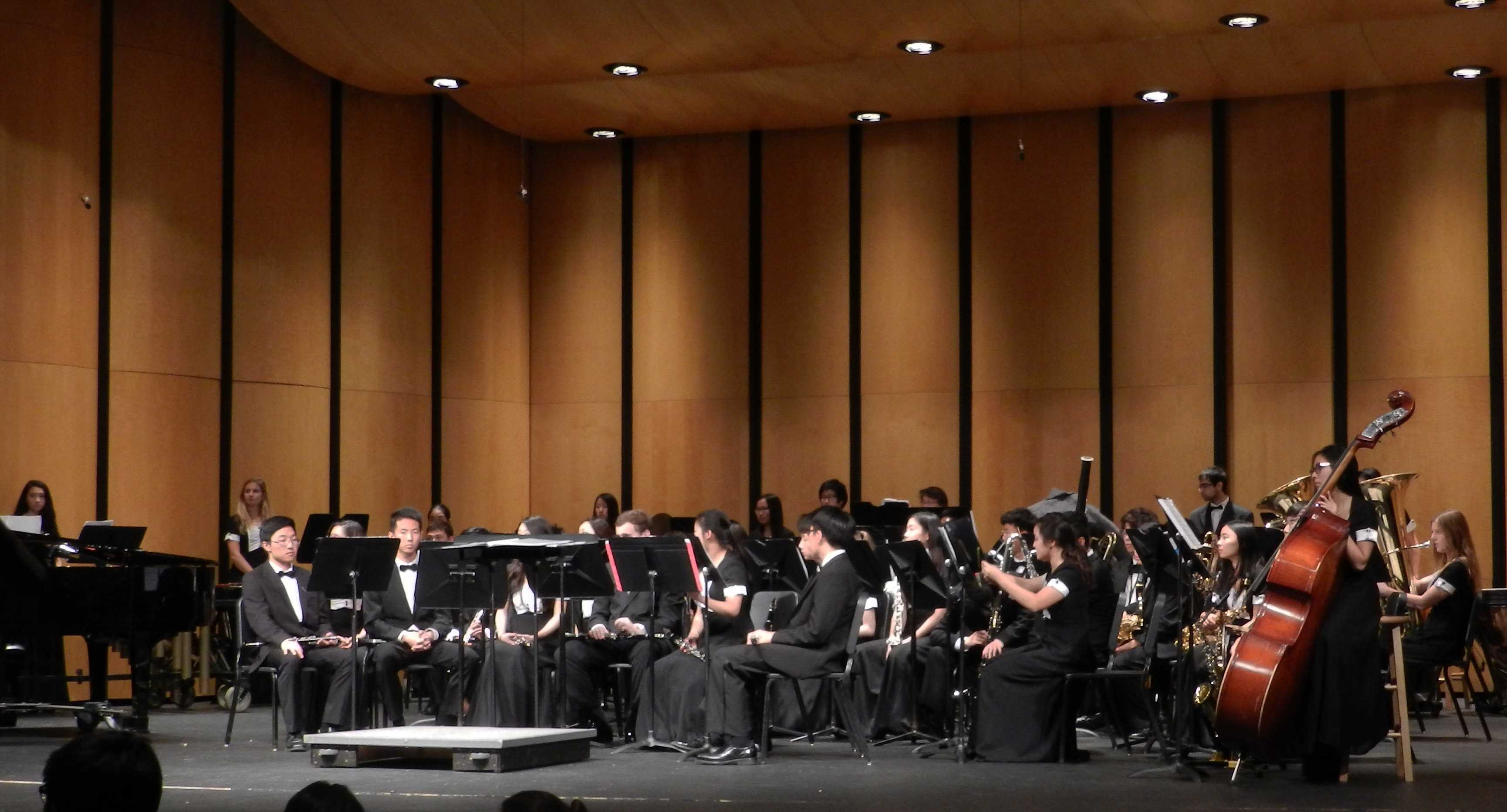 Wind ensemble members take their places as an administrator introduces the piece,