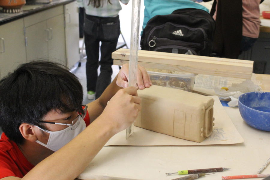 A student carefully measures the dimensions of a clay project.