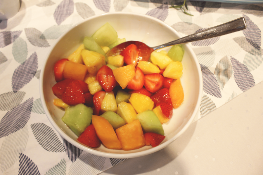 A bowl of fruit salad, with pineapple, strawberries, cantaloupe melon and honeydew melon, all tossed together with a drizzle of honey.