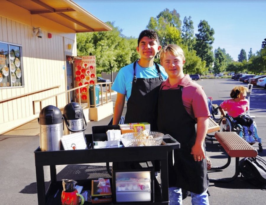 Jude Stamation and Alphonso Sorensen pose alongside the coffee cart in their aprons. Both students are in charge of running the cart and delivering orders twice a week. 