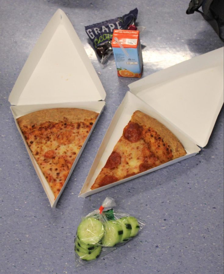 A typical lunch at Woodbridge High consists of a slice of pizza with a fruit or vegetable, such as cucumbers or grapes, and an optional juice box.